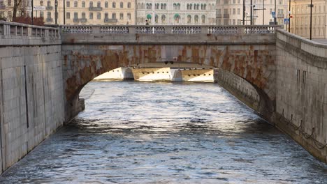 People-walk-on-old-stone-bridge-over-water-stream-in-Stockholm,-centered-static-view