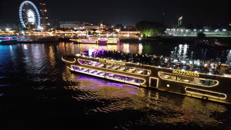 Un-Dron-Sobrevuela-Un-Ferry-Turístico-En-El-Río-Chao-Phraya,-De-Noche,-En-La-Ciudad-De-Bangkok