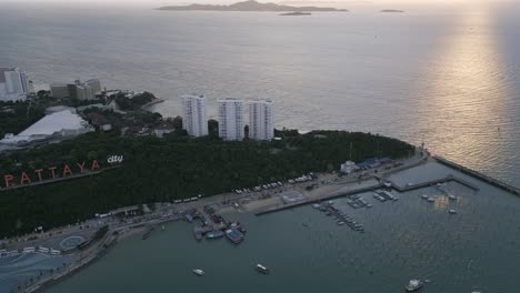 Vista-Aérea-Que-Muestra-Pattaya,-Tailandia,-Al-Atardecer-Con-Vistas-Al-Muelle-Del-Ferry-Y-Al-Cartel-De-La-Ciudad,-Destino-De-Vacaciones-En-La-Isla-De-Ko-Lan