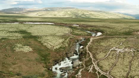 Drone-dolly-above-bubbling-Storula-river-as-water-flows-down-path-around-snow-banks-and-large-rocks-in-Rondane-National-Park-Innlandet-county-Norway