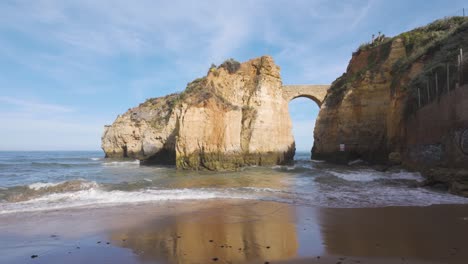 Playa-Praia-Dos-Estudantes-Con-Acantilados-Rocosos-Y-Puente-De-Arco-De-Piedra-En-Lagos,-Algarve,-Portugal