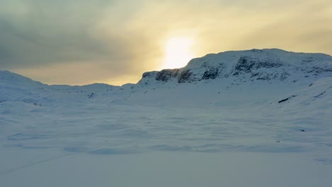 Paisaje-árido-Cubierto-De-Nieve-Del-Paso-De-Montaña-De-Haukelifjell-En-Vinje-Telemark,-Noruega,-Al-Atardecer;-La-Luz-Amarilla-Se-Refleja-En-Las-Nubes-Y-En-La-Nieve