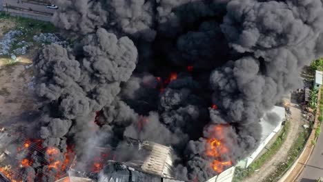 Aerial-shot-of-raging-flames-engulfing-a-chemical-factory,-with-thick-black-smoke-billowing-out