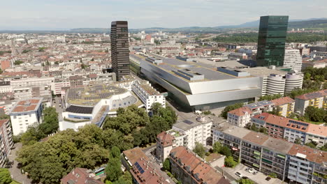 Basel-messe-complex-surrounded-by-buildings-and-greenery-on-a-sunny-day,-aerial-view