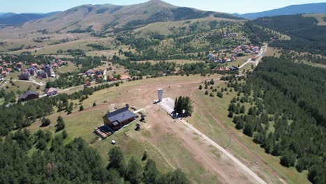 Aerial-view-showcasing-the-Monument-on-Zlatibor-mountain,-Serbia,-with-surrounding-buildings,-scenic-hills,-and-lush-greenery