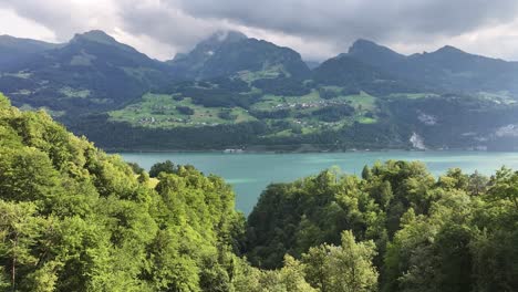 Bosque-Verde-Exuberante-Junto-A-Un-Lago-Azul-Sereno-Con-Majestuosas-Montañas-Bajo-Un-Cielo-Nublado