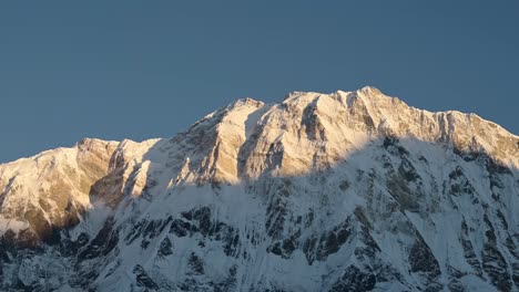 Snowy-Mountain-Ridge-with-Blue-Sky-in-Nepal,-Snowcapped-Mountains-Scenery-in-Snow-with-Steep-Mountain-Face-in-First-Light-at-Dawn-with-Light-on-Top-of-Mountain-in-Himalayas-Mountains-in-Nepal