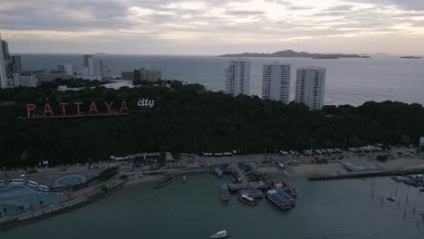 Vista-Aérea-De-Pattaya,-Tailandia,-Al-Atardecer-Con-La-Isla-De-Ko-Lan-A-La-Distancia-Durante-El-Vuelo-Del-Dron-Al-Atardecer-Sobre-El-Muelle-Y-El-Cartel-De-La-Ciudad