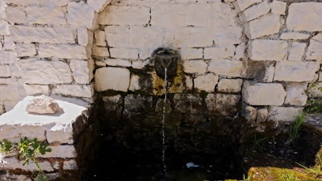 Old-water-fountain-with-a-stone-wall-on-a-sunny-day,-going-forward-and-looking-down