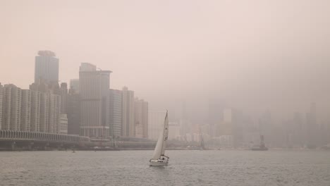 Waterfront-Cityscape-Of-Hong-Kong-City-With-Boat-Sailing-and-Smog-in-Sky,-Wide-Shot