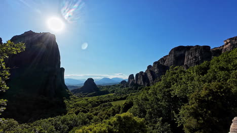 Impresionante-Panorama-De-Los-Acantilados-De-Arenisca-De-Meteora-Y-El-Exuberante-Valle-Bajo-Un-Cielo-Azul-Claro