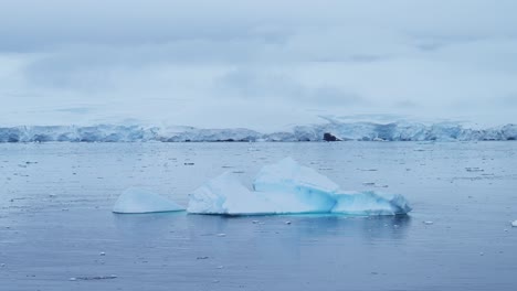 Luftaufnahme-Eines-Eisbergs-Und-Gletschers-In-Der-Antarktis-Mit-Einer-Drohne,-Wunderschöne-Große-Eisberge,-Die-Im-Südlichen-Ozean-In-Ruhigem,-Flachem,-Blauem-Meerwasser-Mit-Landschaftskulisse-Auf-Dem-Festland-Schwimmen