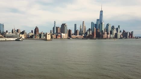 Slow-upward-tilting-drone-shot-of-the-Hudson-River-and-New-York-City-skyline-as-a-boat-passes