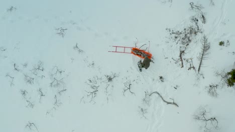 Drone-top-down-rising-view-of-solo-person-in-snowshoes-collecting-sticks-and-placing-in-sled,-Blefjell-mountain-range-Buskerud-Telemark-Norway