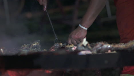 Hands-cutting-massive-beef-ribs-on-the-grill-with-skewer-and-knife-at-night---slow-motion