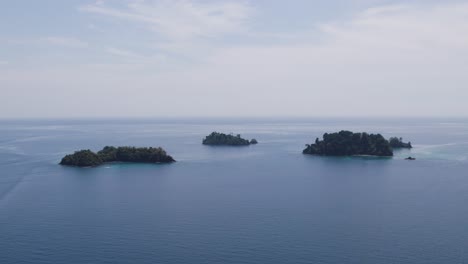 Aerial-tranquil-view-of-multiple-isolated-islands-surrounded-by-calm-waters,-set-under-a-clear-sky-with-a-peaceful,-idyllic-ambiance