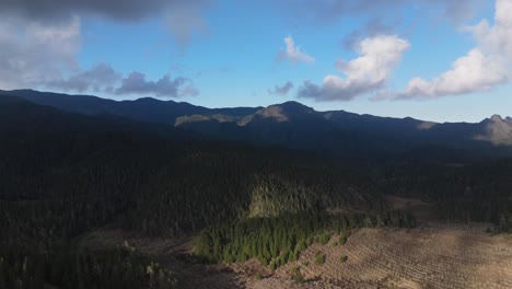 Terraced-clearing-of-forest-on-hillside-with-cloud-shadows-crossing-over-mountains-in-Valle-Nuevo-National-Park,-aerial