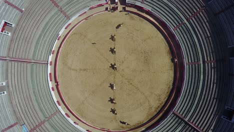 Aerial-view-of-horses-casting-artistic-shadows-on-bull-ring's-arena