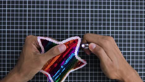 Hands-crafting-a-colorful-sequin-star-with-rainbow-pattern-on-a-grid-background