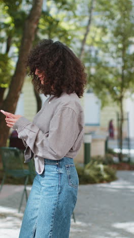 Touristin,-Junge-Frau-Mit-Lockigem-Haar,-Die-Mit-Dem-Smartphone-Textnachrichten-Eingibt-Und-Auf-Der-Karte-Nach-Einem-Weg-Sucht