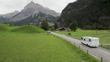 Camper-drives-through-lush-green-valley-with-mountain-backdrop