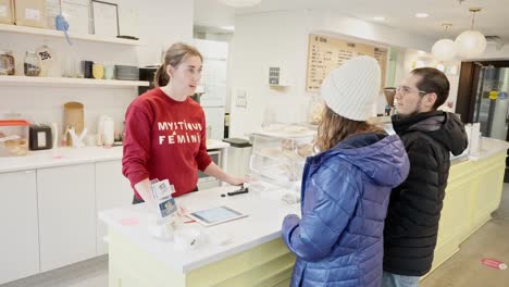 Una-Pareja-Diversa-Pide-Helado-A-Una-Mujer-Joven-Con-Un-Suéter-Rojo-En-Una-Tienda