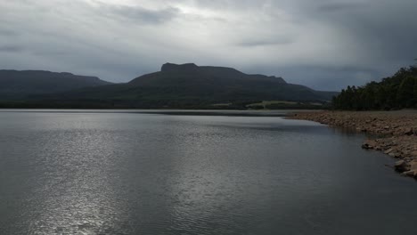 Drone-flying-at-low-altitude-over-Huntsman-Lake-waters-on-cloudy-day,-Tasmania-island-in-Australia