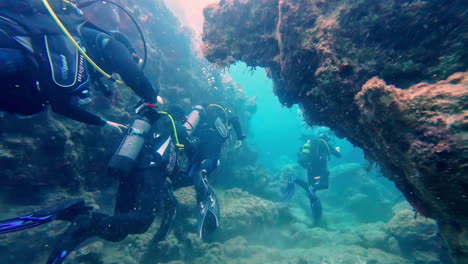 Group-of-scuba-diver-exploring-the-under-water-world-together-between-corals-and-sea-life,-slow-motion