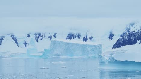 Iceberg-Flotando-En-El-Océano-En-El-Mar-Con-Montañas-De-La-Antártida-En-La-Costa-De-La-Península-Antártica,-Hermoso-Paisaje-Costero-Azul-Dramático-Y-Paisaje-Marino-En-Una-Escena-De-Mar-De-Invierno-Helado-Con-Hielo