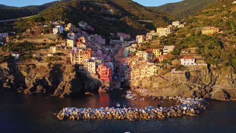 Wide-drone-aerial-orbit-over-the-sea-with-complete-perspective-of-the-colourful-bay-of-Riomaggiore-on-the-Ligurian-Coast-in-Italy-during-sunset-and-golden-hour