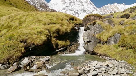 Waterfall-Stream-and-Himalayas-Mountains-in-Nepal,-Snowcapped-Mountain-Top-Landscape-and-Flowing-River-Scenery-in-High-Altitude-Terrain-in-Annapurna-Region-at-Annapurna-Base-Camp