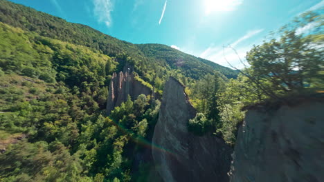 Piramidi-di-terra-di-segonzano-in-a-lush-green-landscape-under-a-bright-blue-sky,-aerial-view