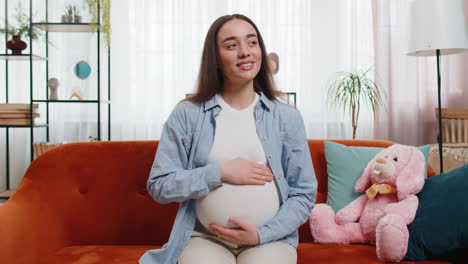 Retrato-De-Una-Futura-Madre-Sonriente-Sentada-En-Un-Sofá-Tocando-Su-Barriga-Embarazada-Esperando-Un-Bebé-En-Casa