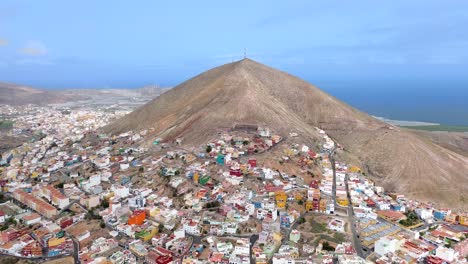 Aerial-view-of-Galdar-town-city-village-under-the-mountain-against-seascape-in-Gran-Canaria,-Spain