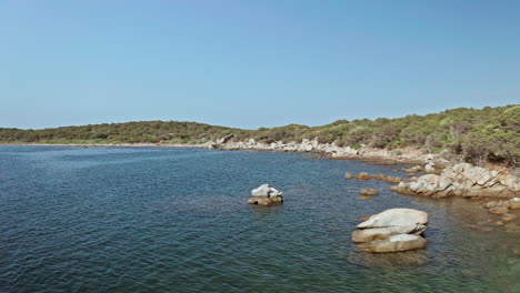 Crystal-clear-blue-waters-and-rocky-shoreline-of-Sardinia-under-a-bright-blue-sky