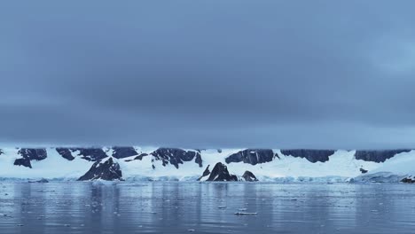 Paisaje-Costero-De-Montañas-Invernales-En-La-Antártida,-Nubes-Dramáticas-Y-Cielo-En-Un-Paisaje-Azul-Oscuro-Frío-Con-Glaciares-Y-Agua-De-Mar-En-La-Costa,-Paisaje-Marino-De-La-Península-Antártica-En-Una-Escena-Atmosférica-Melancólica