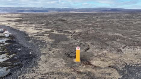 Das-Video-Zeigt-Eine-Atemberaubende-Luftaufnahme-Eines-Leuchtturms-An-Der-Küste-Islands,-Umgeben-Von-Schwarzem-Sand,-Felsigem-Gelände-Und-Majestätischen-Bergen-In-Der-Ferne