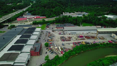 Aerial-view-of-an-industrial-area-in-Pittsburgh,-Pennsylvania,-featuring-warehouses,-machinery,-and-nearby-greenery-under-a-cloudy-sky