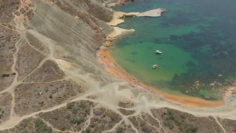 Vista-Aérea-De-Los-Acantilados-De-Arcilla,-La-Bahía-De-Qarraba,-La-Playa-Y-Los-Barcos-En-El-Océano-Azul-Claro-En-Verano-En-Malta