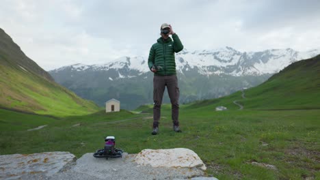 Mann-Mit-FPV-Brille-Steht-Vor-Alpiner-Landschaft,-Fliegt-Drohne-Mit-Angebrachter-Insta360-Go-Actionkamera