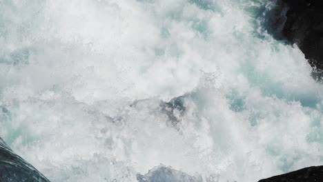 Close-up-of-a-cascading-waterfall,-with-whitewater-tumbling-and-splashing-over-the-dark-rocky-ledges-into-a-pool-below