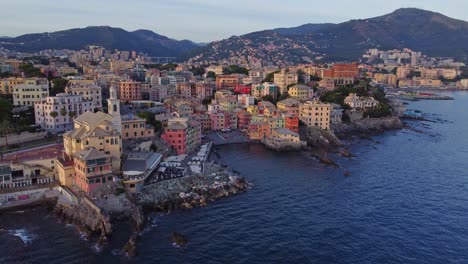 Órbita-Aérea-De-Un-Dron-Sobre-La-Playa-De-Boccadasse,-Génova,-Durante-La-Puesta-De-Sol-Y-La-Hora-Dorada,-Que-Muestra-Edificios-Coloridos,-El-Mar,-La-Bahía-Y-Una-Iglesia