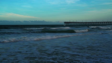 Ocean-or-sea-waves-time-lapse-with-a-wooden-pier-walkway-on-the-horizon-at-dusk