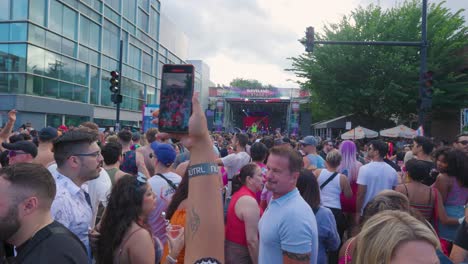 Eine-Frau-Hält-Ein-Smartphone-Hoch-Und-Filmt-Eine-Lebhafte-Menge-Beim-Gay-Pride-Festival,-Die-Unter-Dem-Sommerhimmel-Feiert.-Die-Mit-Regenbogenmustern-Geschmückte-Menge-Versammelt-Sich-Unter-Freiem-Himmel,-Um-Beim-Gay-Pride-Zu-Feiern.