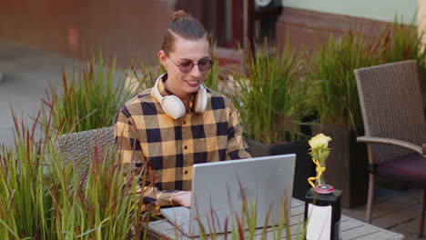 Happy-young-man-tourist-working-online-distant-job,-laptop-netbook-in-city-street-cafe-restaurant