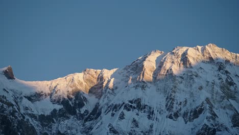 Snowy-Mountain-Ridge-with-Blue-Sky-in-Nepal,-Snowcapped-Mountains-Scenery-in-Snow-with-Mountain-Face-in-First-Light-at-Dawn-with-Light-on-Top-of-Mountain-in-Himalayas-Mountains-in-Nepal-at-Annapurna