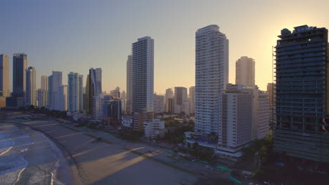 Amanecer-Atravesando-Edificios-En-Playa-Boca-Grande,-Cartagena-De-Indias,-Colombia