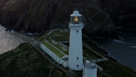 South-Stack-lighthouse-aerial-view-circling-island-nautical-beacon-below-mountain-shore-at-dusk