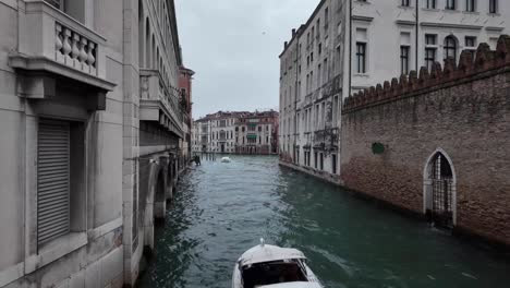 Toma-Reveladora-De-La-Vista-De-La-Calle-Del-Canal-De-Venecia-Con-Agua-Fluyendo-Y-Una-Lancha-Rápida-Moviéndose-En-Ella,-Rodeada-De-Edificios-Históricos-Que-Tienen-Puertas-De-Entrada-En-Forma-De-Arco.