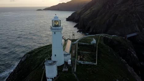 Luftaufnahme-Des-Leuchtturms-South-Stack,-Der-In-Der-Abenddämmerung-Die-Insel-Umkreist,-Ein-Nautisches-Leuchtfeuer-Unter-Dem-Berg